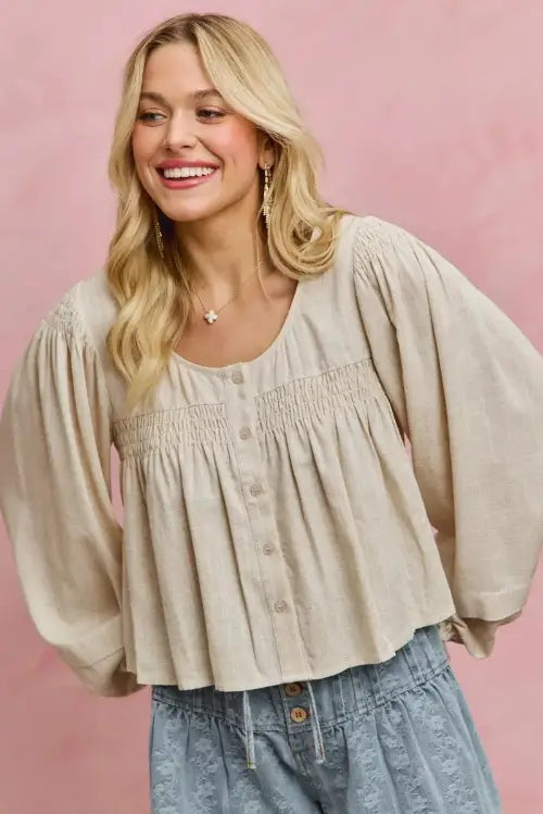 Woman wearing a beige blouse with balloon sleeves against a pink background