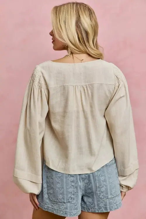 Back of Woman wearing a beige blouse and denim shorts against a pink background
