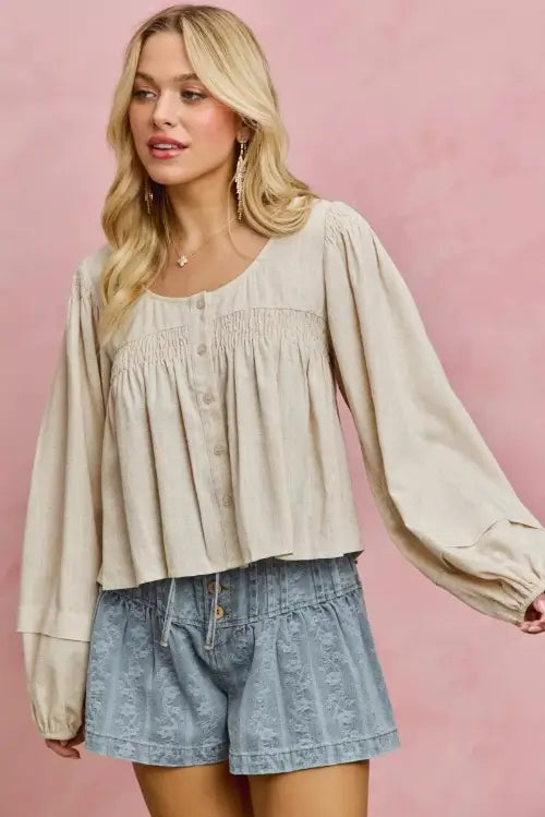 Woman wearing a beige blouse and denim shorts against a pink background