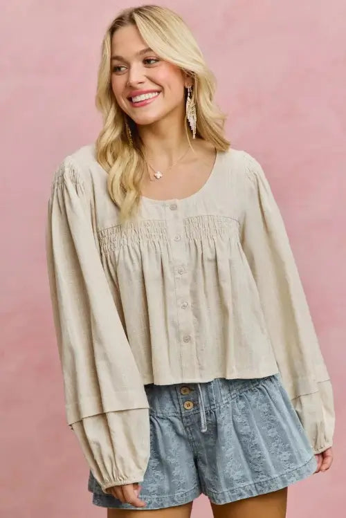Woman wearing a beige blouse and denim shorts against a pink background