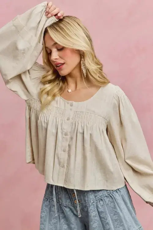 Woman wearing a beige blouse and denim shorts against a pink background