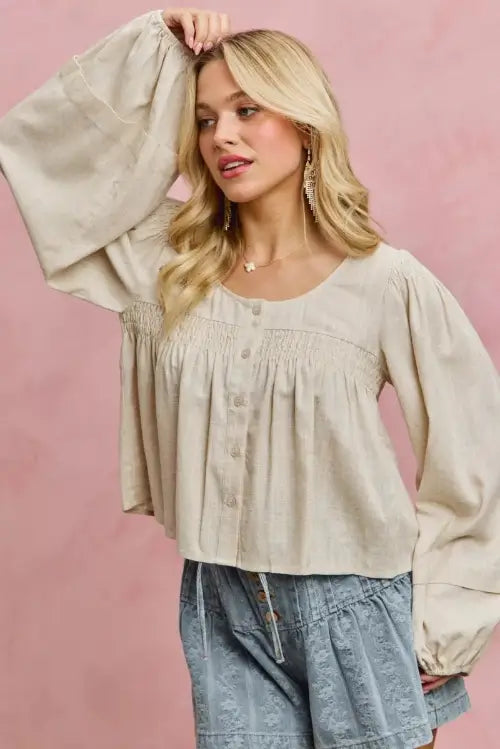 Woman wearing a beige blouse with long sleeves against a pink background