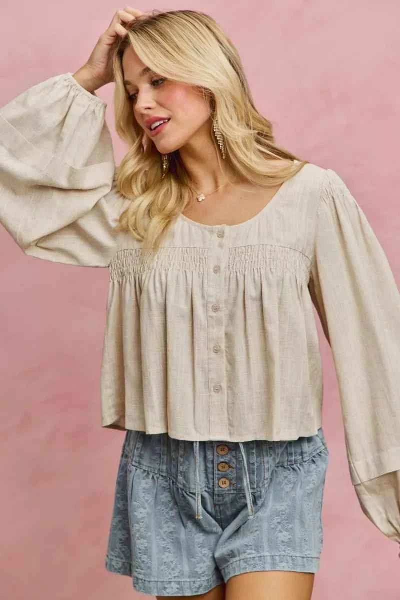 Woman wearing a beige blouse and denim shorts against a pink background