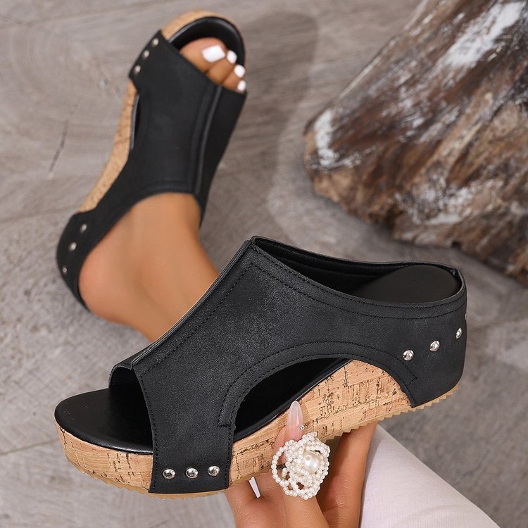 Black open-toe sandals with cork sole worn by a person, on a neutral background.