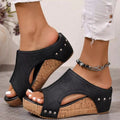 Black wedge sandals with cork sole worn by a person on a neutral background