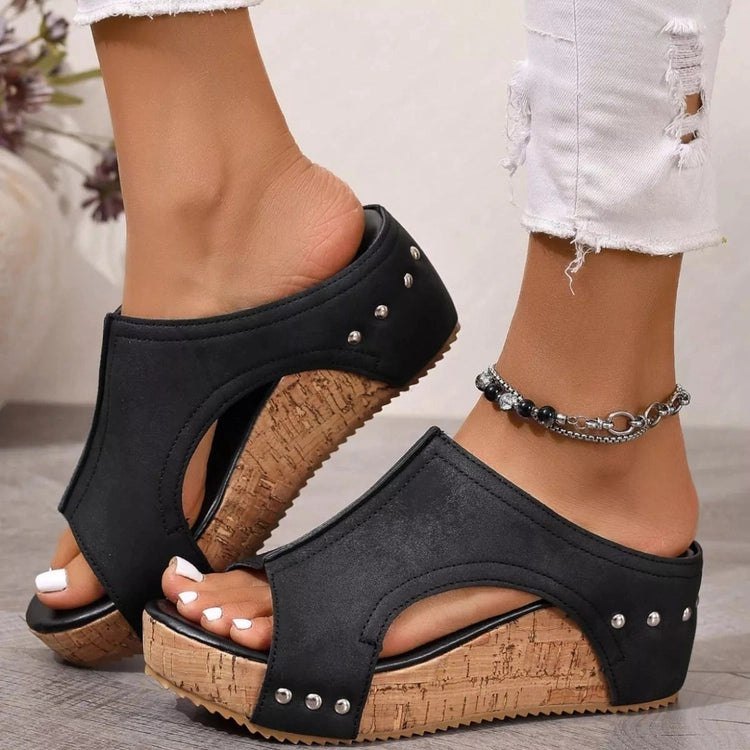 Black wedge sandals with cork sole worn by a person on a neutral background