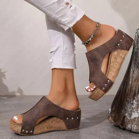 Brown open-toe sandals with cork wedge sole worn by a person in white jeans.