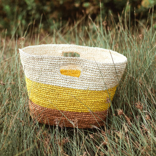 Woven basket with yellow and white design in a grassy field