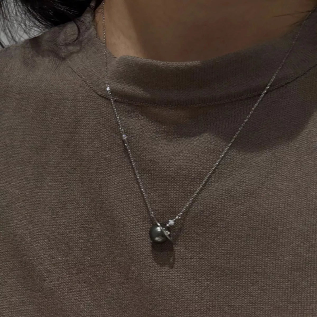 Necklace with a pendant on a person wearing a brown turtleneck.