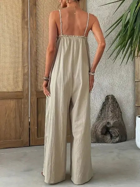 Woman wearing a beige jumpsuit standing in a room with wooden panels and a plant.