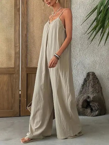 Woman wearing a light-colored jumpsuit standing against a neutral wall with a wooden door and plant in the background.
