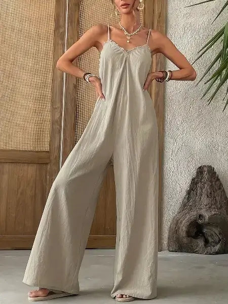 Woman wearing a light-colored jumpsuit standing against a textured wall.