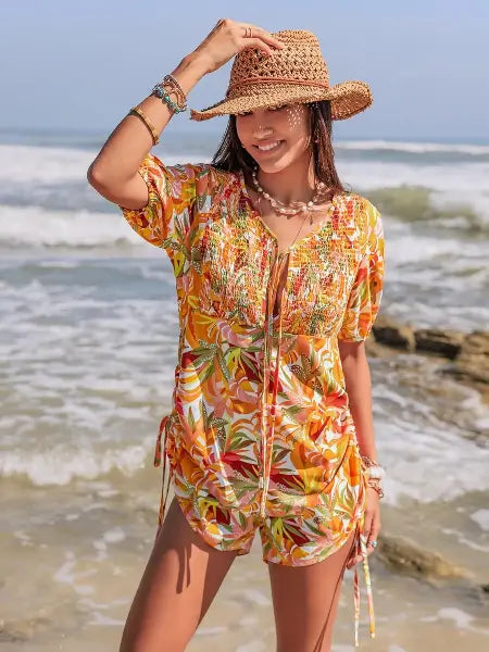 Woman in a colorful dress and straw hat standing on a beach.