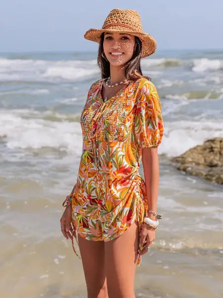 Woman in a colorful floral dress and straw hat standing on a beach.