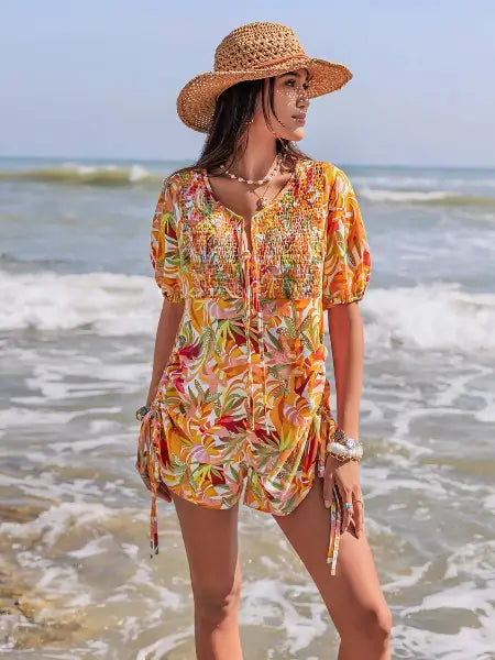 Woman in a colorful floral dress and straw hat standing on a beach.
