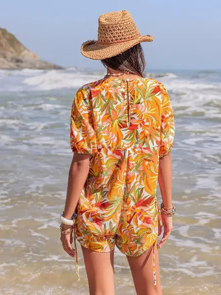 Person wearing a colorful floral dress and straw hat on a beach