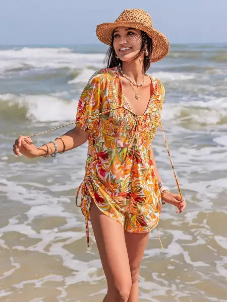 Woman in a colorful dress and straw hat standing on a beach with ocean waves in the background