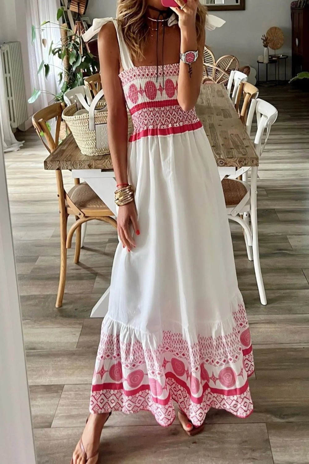 Woman wearing a white dress with red and pink patterns in a room with wooden flooring.