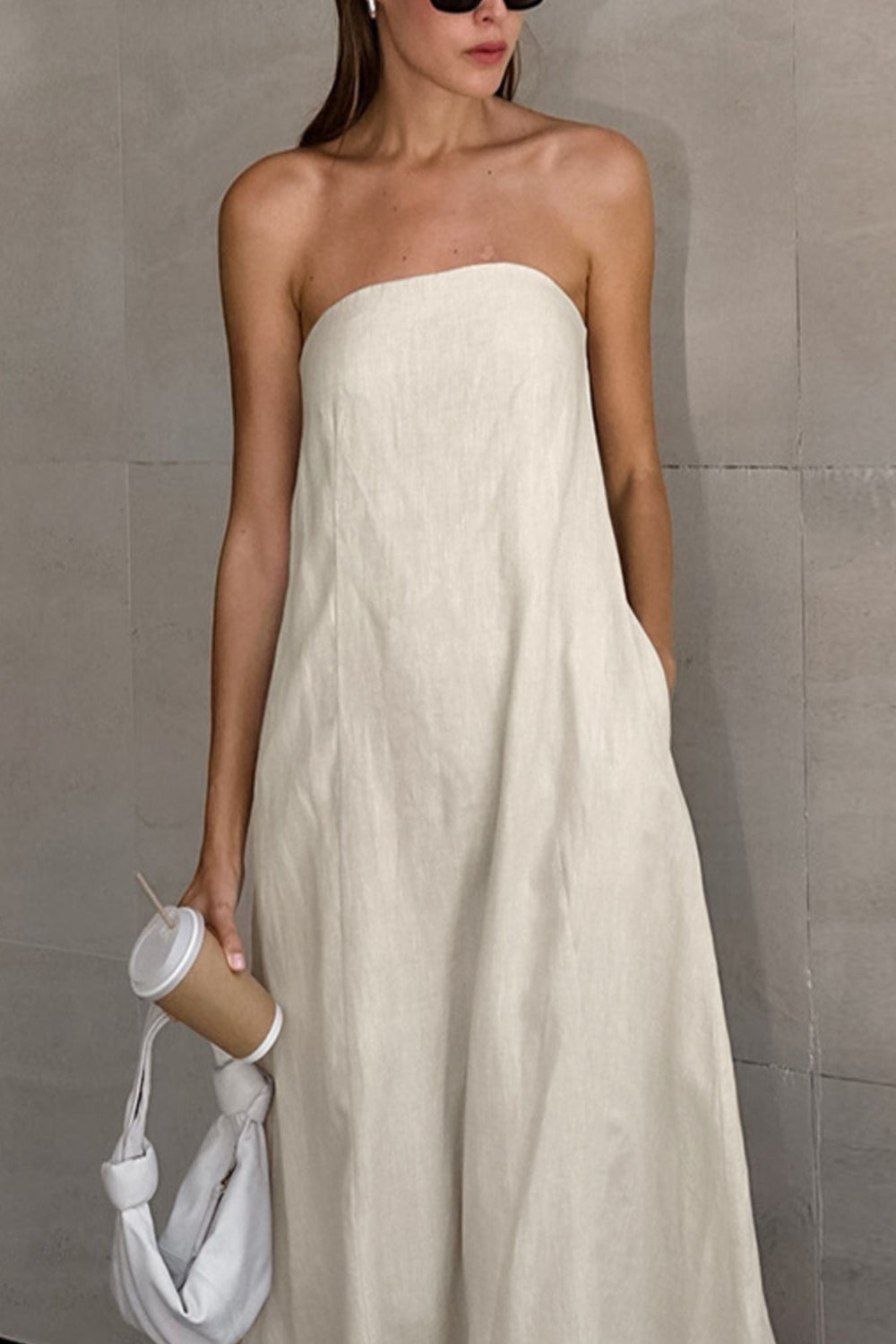 Smocked Back Tube Dress - Salty Season LLC Woman wearing a strapless white dress holding a white bag and a coffee cup against a gray wall.