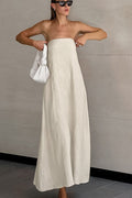 Woman wearing a strapless white dress holding a white handbag against a plain background