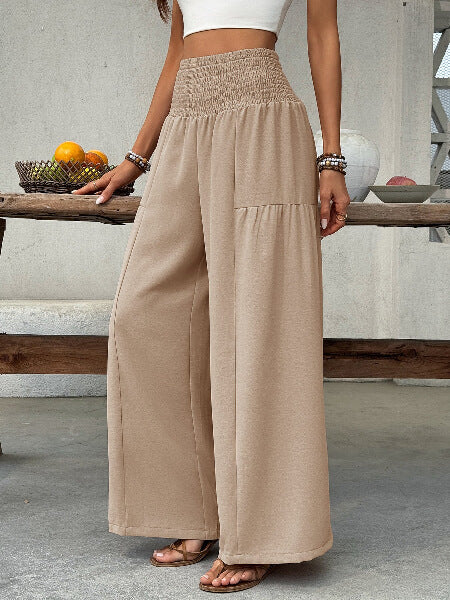 Person wearing beige wide-leg pants standing in a casual setting with a wooden table and fruit bowl.
