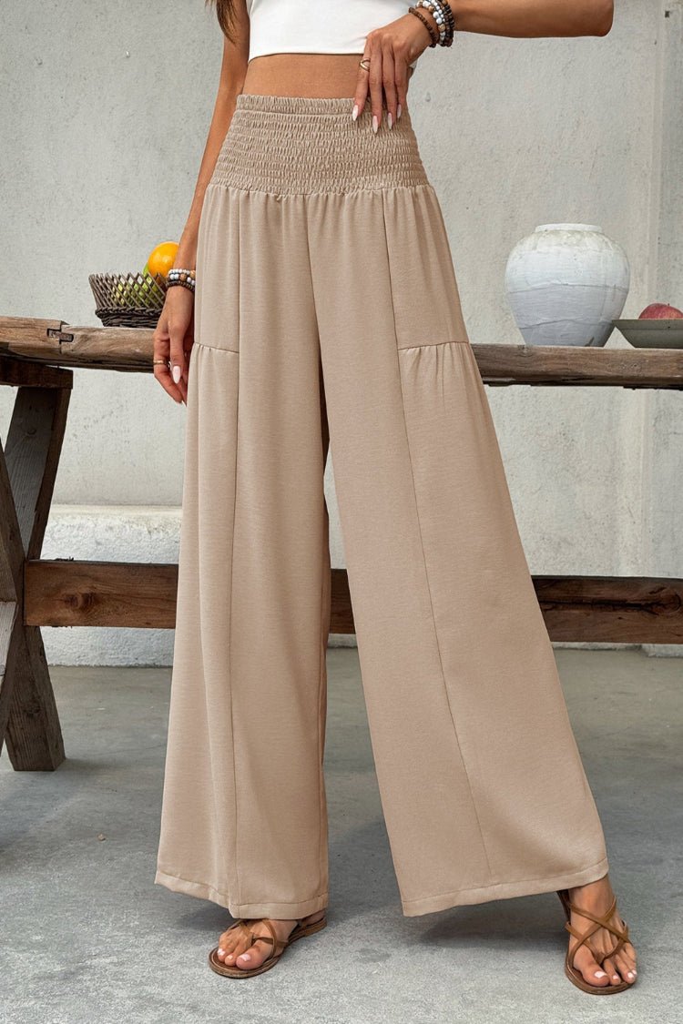 Person wearing beige wide-leg pants in a casual setting with a wooden table and decorative items.