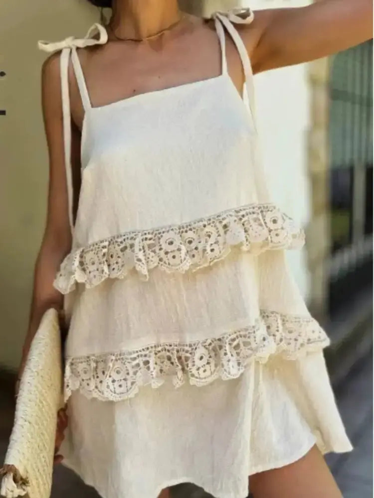 A woman wearing a cream-colored cotton camisole dress with tie straps, featuring two tiers of ruffles decorated with intricate crochet lace. She is holding a woven straw clutch bag.