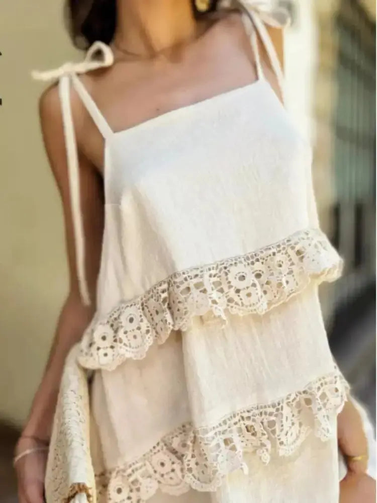 A woman wearing a cream-colored cotton camisole top with delicate crochet lace ruffle trim and tie straps.