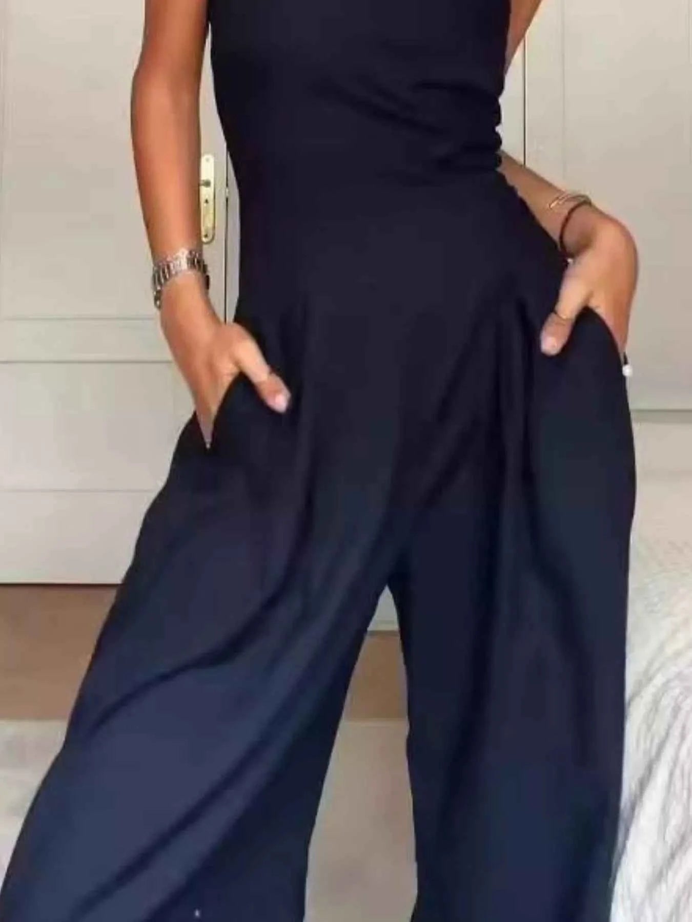 Person wearing a black jumpsuit with wide-leg pants in an indoor setting.