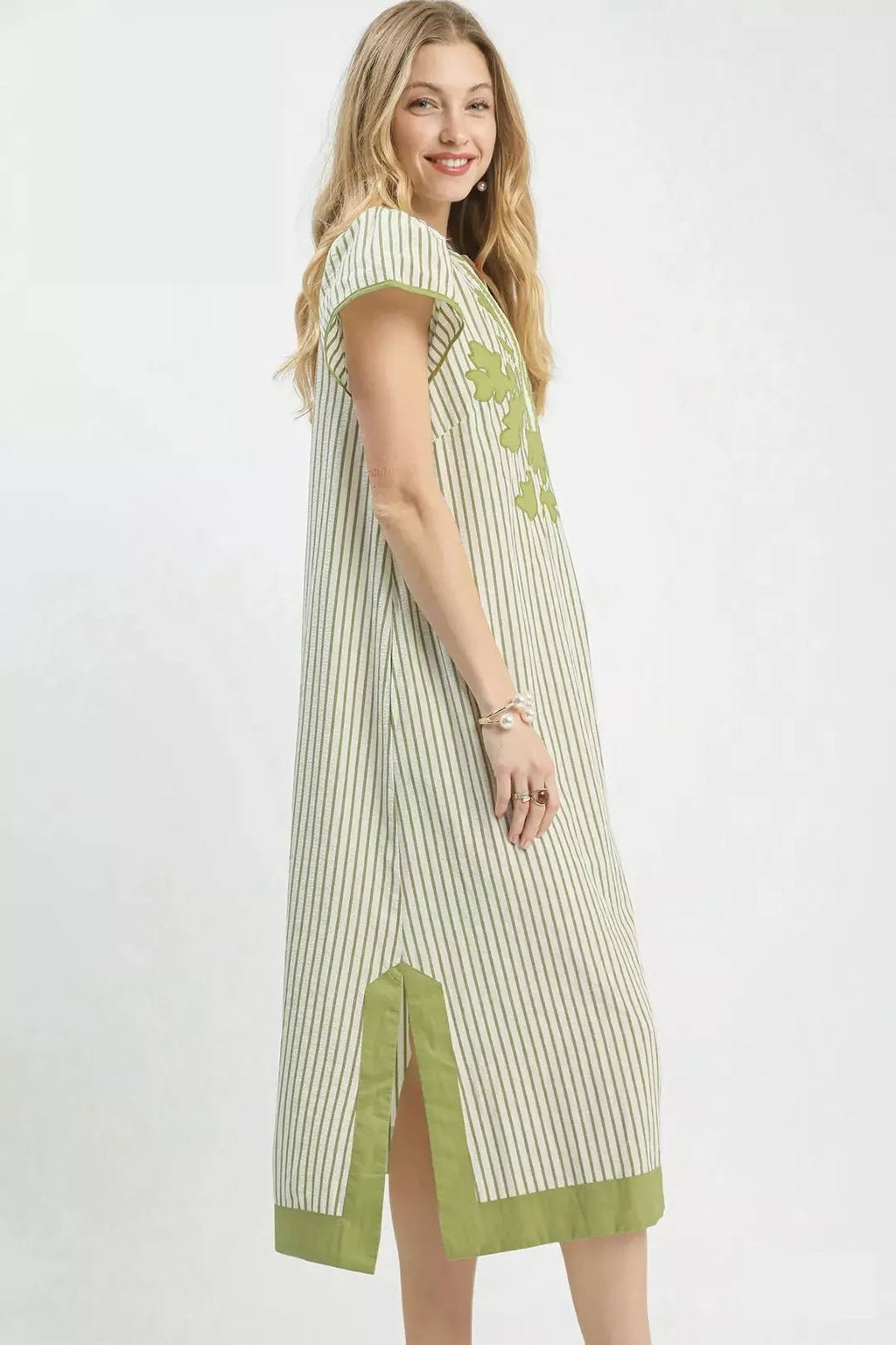 Woman wearing a green and white striped dress with floral details on a white background