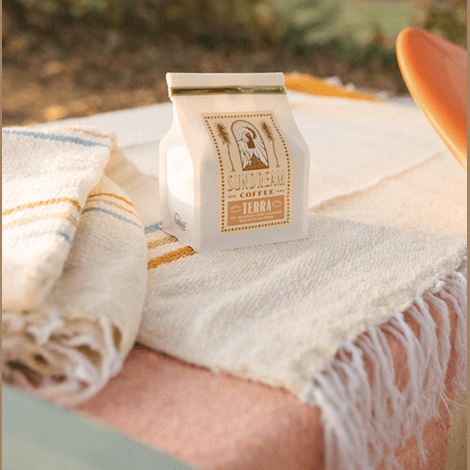 Sundream Sunrise striped cotton throw with white fringe next to coffee bag
