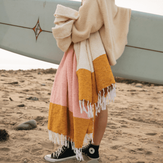 Mustard and pink upcycled cotton beach blanket draped over surfboard shoulder