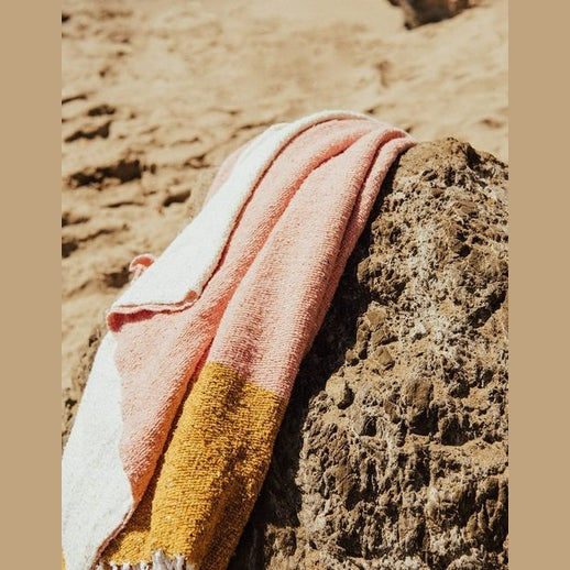 Folded mustard cream pink eco-friendly cotton blanket draped on beach rock