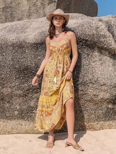 Woman in a floral dress and hat standing against a rocky background