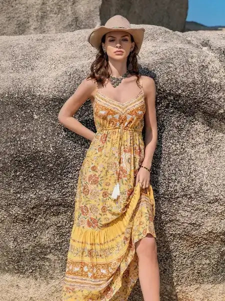 Woman in a floral dress and hat standing against a rocky background