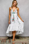 Woman wearing a white dress with floral embroidery against a gray background