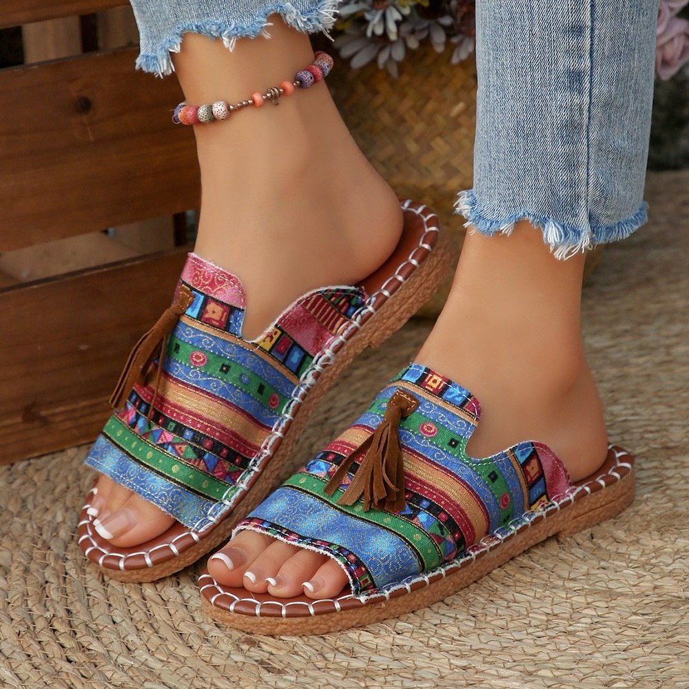 Colorful patterned sandals worn with denim jeans on a woven surface.