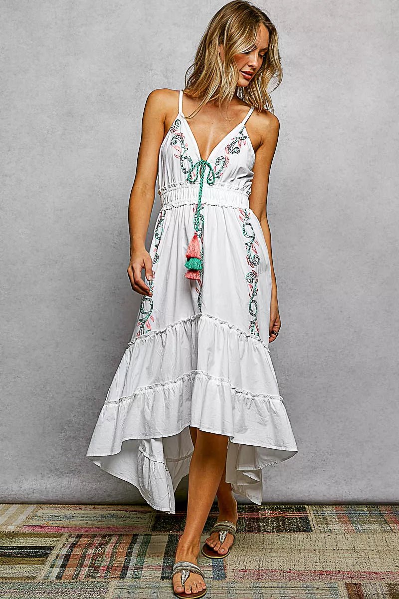 Woman wearing a white dress with floral embroidery against a gray wall.