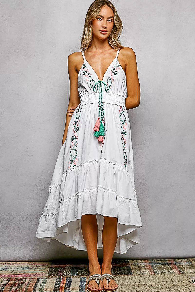 Woman wearing a white dress with floral embroidery against a gray background