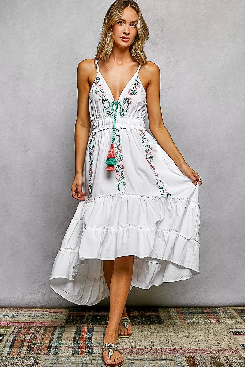 Woman wearing a white dress with floral embroidery against a gray background
