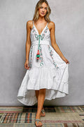 Woman wearing a white dress with floral embroidery against a gray background