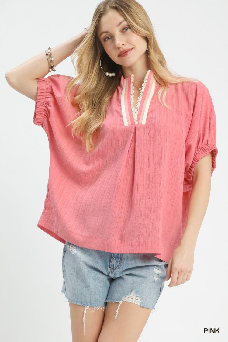 Woman wearing a pink blouse with lace details and denim shorts on a white background