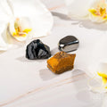 Raw protection stones set with black obsidian, hematite, and tiger's eye on wood with orchid petals
