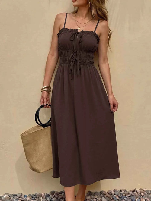 Woman wearing a brown dress holding a beige bag against a beige background