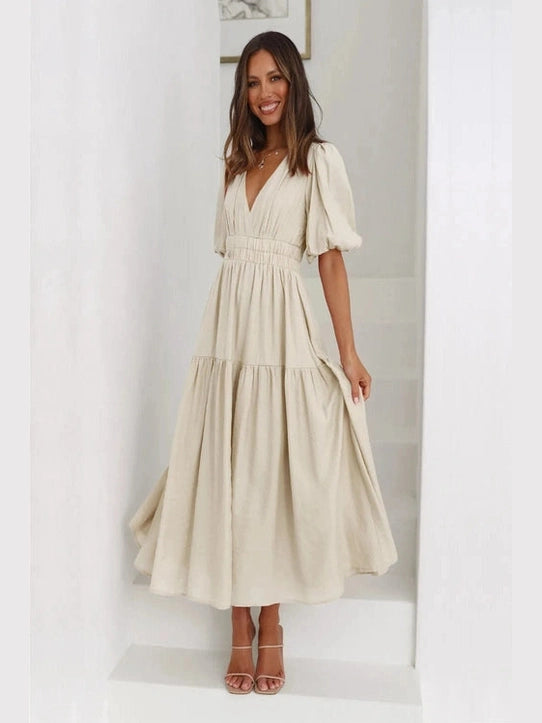 Woman wearing a beige dress with puff sleeves in a minimalistic room.