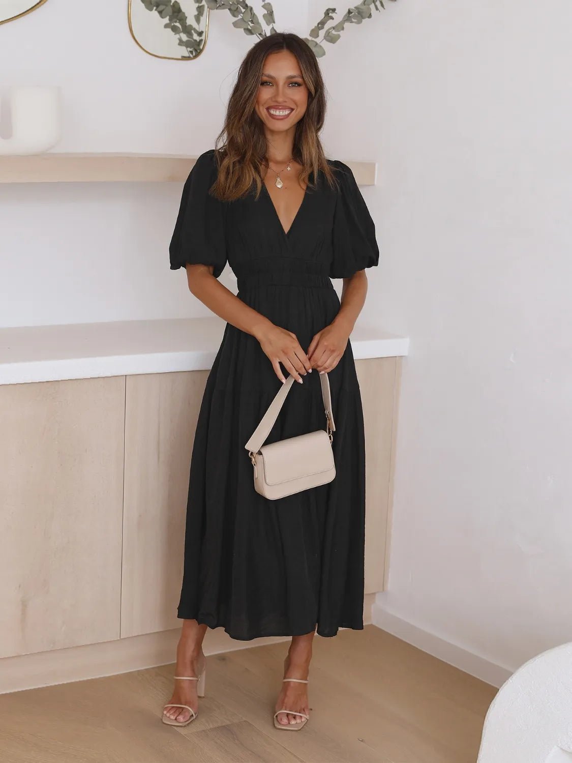 Woman in a black dress holding a beige handbag in an indoor setting