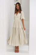 Woman wearing a beige dress with puff sleeves in a minimalistic room.