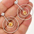 Silver hoop earrings with yellow gemstones held in a hand against a white background