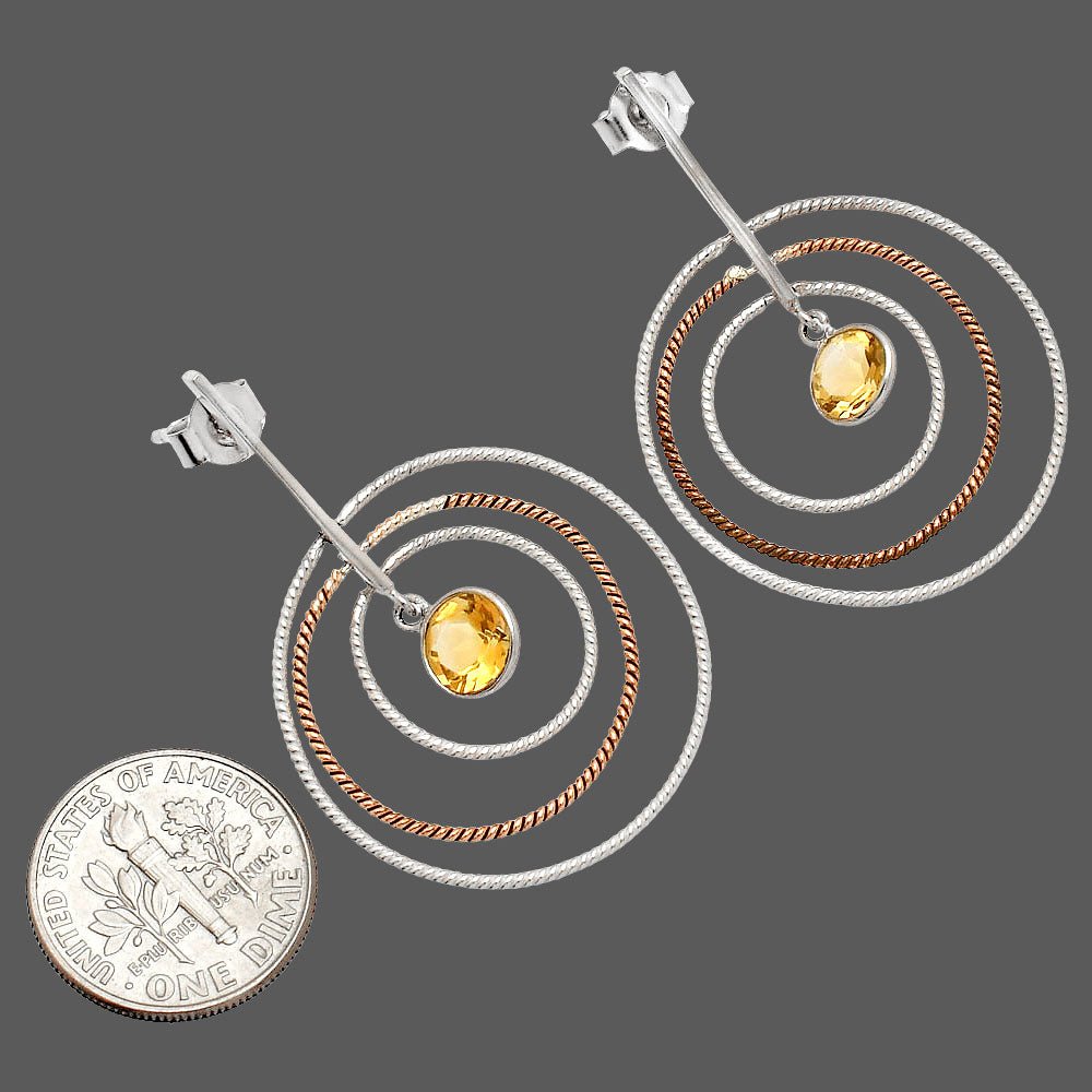 Pair of spiral earrings with yellow gemstones and a quarter for scale on a gray background