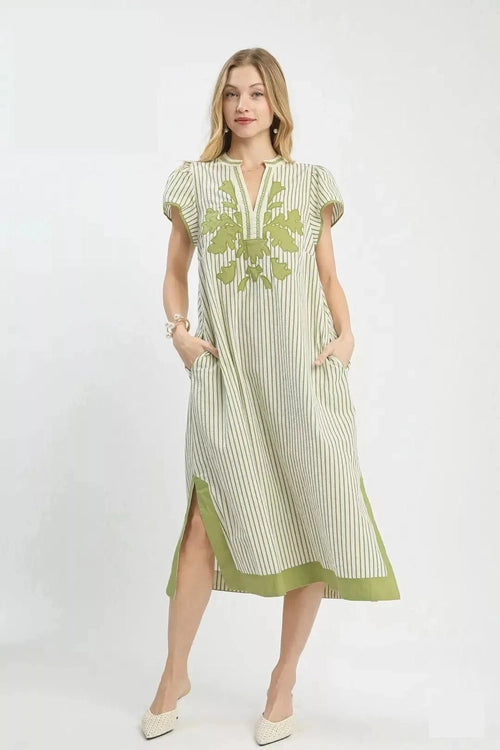 Woman wearing a green and white striped dress with floral embroidery on a white background